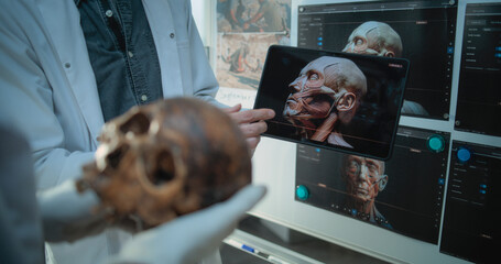 Scientists study anatomy of fossil skull using tablet computer with created 3D model of Neanderthals, work in archaeological laboratory. Board with printed images of ancient humans in the background.