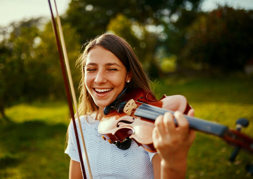 Girl, violin and happy in nature for music, talent and entertainment for event. Musician, string instrument and smile on grass for art, rehearsal and practice for creativity with skill development