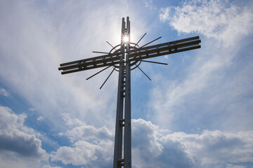 The sun shining through behind the cross against the blue sky.