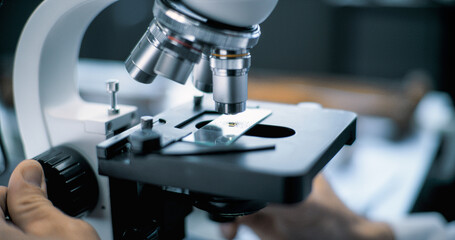 Close up of microbiologist or chemist putting fossil specimen under microscope for analysis....