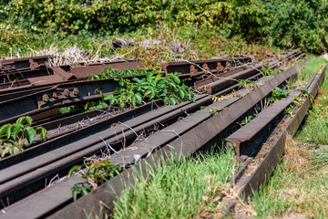 teren rozbiórki stare zardzewiałe i rozebrane tory kolejowe leżące na zielonej trawie w tle krzaki © DP.REPORT
