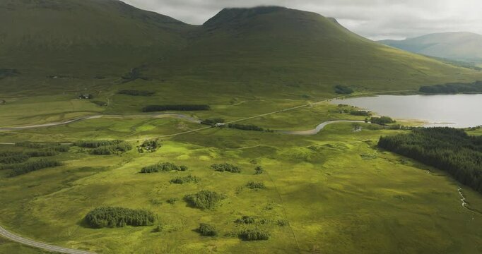 Aerial view of beautiful Loch Tulla surrounded by lush mountains and winding road, Bridge of Orchy, United Kingdom.