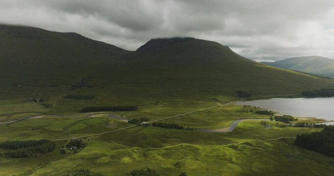 Aerial view of tranquil Loch Tulla surrounded by majestic mountains and a winding road, Bridge of Orchy, United Kingdom.