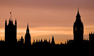 Silhouette of London landmarks Houses of Parliament and Big Ben against a vibrant sunset sky in early evening. Historic buildings contrasted against a stunning sunset sky.