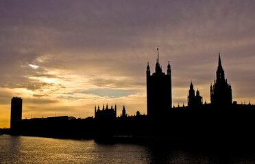 Silhouette of Houses of Parliament building against a sunset sky over the Thames river in London during twilight. A vibrant sunset sky, reflecting over the river. 