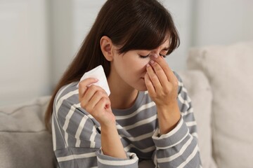 Woman with napkin suffering from sinusitis on sofa at home