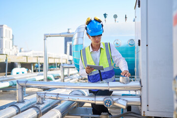 Fototapeta premium Technician working on tablet and checking pipeline valves or water tank area at urban industrial site
