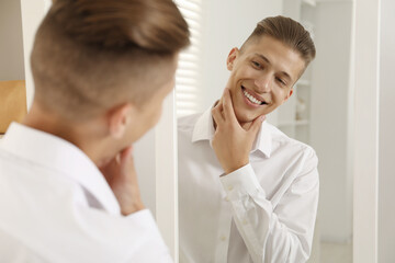 Fototapeta premium Handsome man in shirt looking at mirror indoors