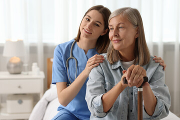 Fototapeta premium Smiling healthcare worker supporting senior patient on bed indoors. Space for text