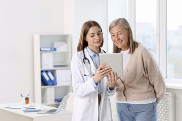 Fototapeta premium Smiling healthcare worker and senior patient checking analysis results on tablet in hospital. Space for text