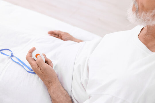 Senior man pressing emergency call button on bed in hospital, closeup