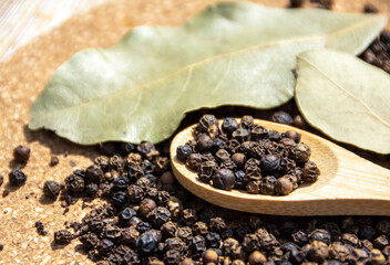 Dry spice black peppercorns on a wooden spoon and dried bay leaf. Spices and seasonings, cooking