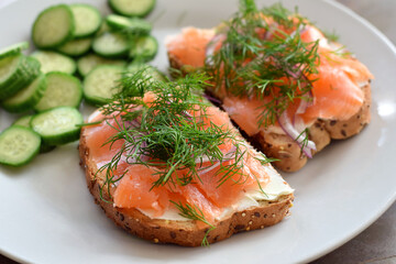 Multigrain bread toast with smoked salmon garnished with fresh dill and side sliced cucumbers