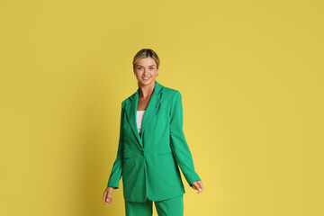 Beautiful woman in stylish green suit on yellow background