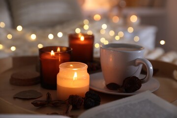 Burning candles, lights, coffee and decor on bed indoors, closeup. Autumn atmosphere