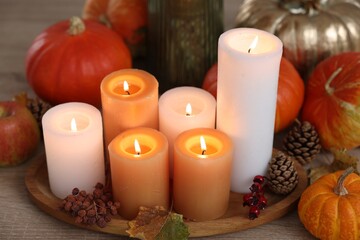 Tray with many burning candles and autumn decor on wooden table, closeup