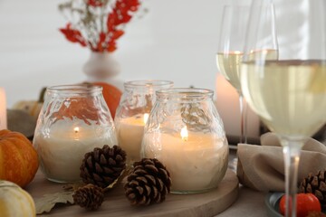 Burning candles, glasses of wine and autumn decor on table, closeup