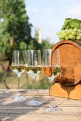 Tasty wine in glasses, grapes and barrel on wooden table outdoors