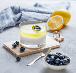 Creamy lemon panna cotta with blueberries in a glass on a wooden board with fresh berries and...