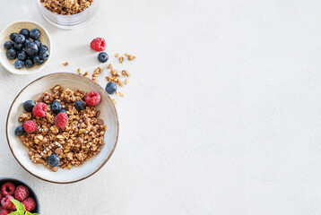 Dry muesli or granola, raspberries and blueberries in a bowl on a light background with fresh berries and morning sunlight.