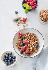 Flat lay of granola, raspberries and blueberries in a bowl on a light background with fresh berries and morning sunlight.