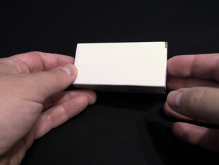 Close-up shot of a caucasian person's hands holding a small white box against a black background. For mockup, copy space, template