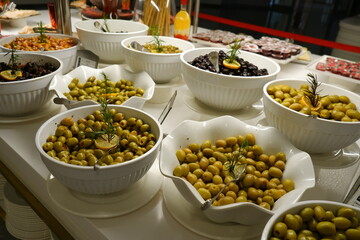 A variety of green and black olives presented in bowls at a buffet table, garnished with lemon slices and rosemary sprigs for a fresh look.
