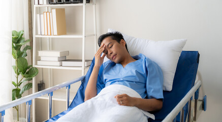 Patient Resting in Hospital Bed: A young man in a hospital gown lies in bed, resting his head on...