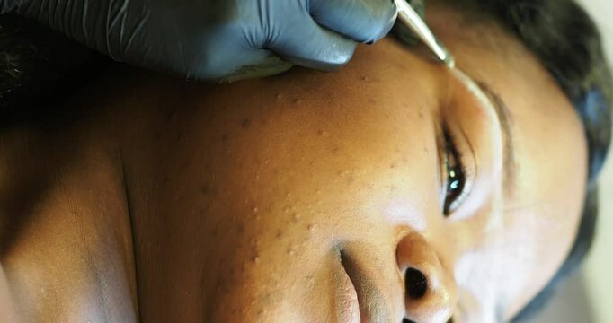 Beautician drawing white correction lines for eyebrow permanent tattoo on young black woman