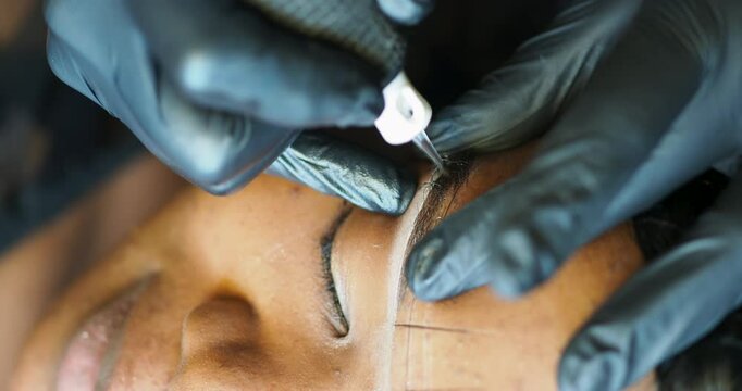 Beauty therapist apply permanent makeup to client eyebrows in salon using rotary pen tattoo machine