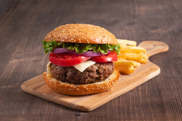 Homemade delicious hamburger with beef, onion, tomato, lettuce and cheese. Fresh burger close up on wooden rustic table with potato fries. Cheeseburger. Burger.