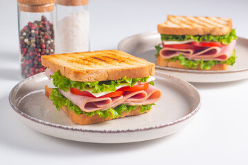 Close-up of two sandwiches with bacon, salami, prosciutto and fresh vegetables on rustic wooden cutting board. Club sandwich concept