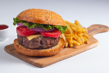 Homemade delicious hamburger with beef, onion, tomato, lettuce and cheese. Fresh burger close up on wooden rustic table with potato fries. Cheeseburger. Burger.