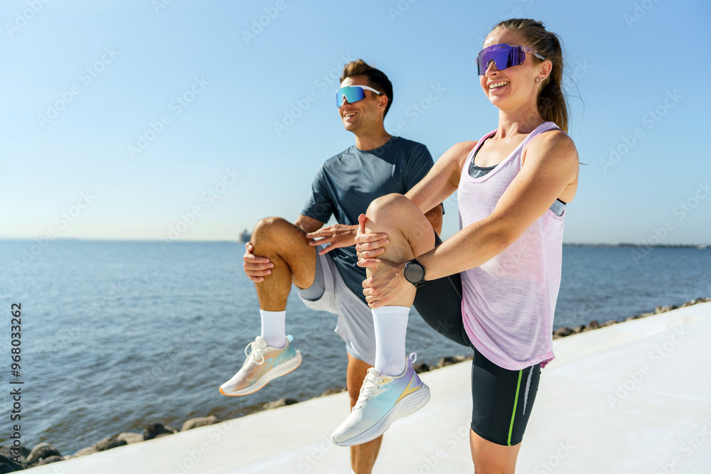 Wall mural a man and woman smile while performing knee lifts, warming up for their workout by the water on a su