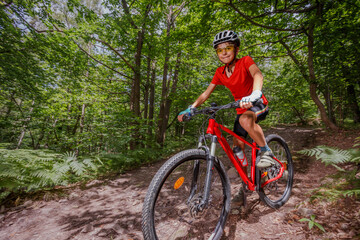 Naklejka premium Happy mountain cyclist teenager on sunny summer forest trail