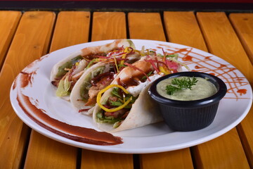 long platter of tacos with a bowl of salsa. Tacos Dorados: Rolled, fried tacos typically filled with shredded chicken or potatoes, served with salsa and crema.