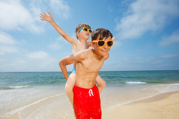 Happy piggyback ride with big brother in sandy beach at summer