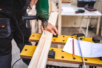 Unrecognizable male carpenter using electric drill on a wooden plank outdoors