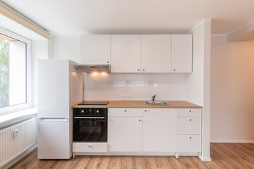 Fototapeta premium Scandinavian Style Cozy Modern Open Bright Minimalism Kitchen Home Interior. Oven, Faucet, Fridge and Furniture in Background. Dark Brown Flooring. White Cabinets