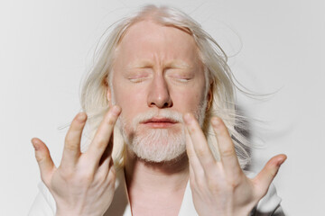 Portrait of a serene individual with long white hair and beard, closed eyes, against a plain white...
