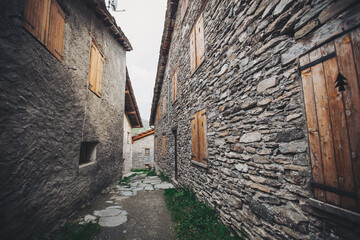 antique wooden window on a construction made of slate, typical of the villages of architecture in the province of Alps Mountains. Closed wooden window shutters with with typical alpine decoration