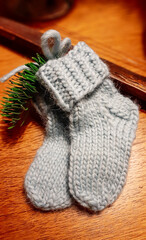 Children's hands made socks of natural gray wool, with a green pine branch on a wooden surface. A christmas gift made with love and own hands.