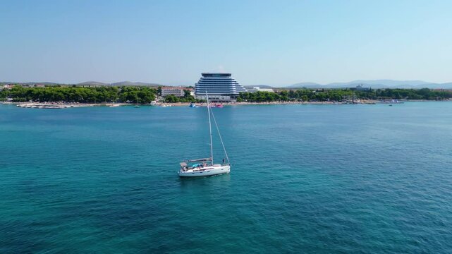 A sleek yacht cruising near the coastal town of Vodice, Croatia, captured from the air. The yacht glides through the crystal-clear waters of the Adriatic Sea, creating a picturesque scene