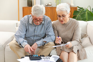 Middle aged senior couple sit with laptop and paper document. Older mature man woman reading paper...