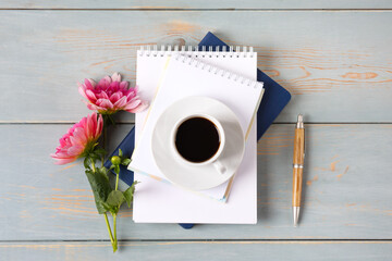 Artistic composition with opened blank notepad and pen, cup of black coffee, pink dahlias flower on blue wooden table. Festive office desktop concept. Morning coffee cup.