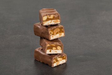 Energy bar. Nougat, caramel with peanuts, in milk chocolate. Dark gray background. Close-up