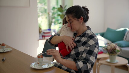 Mother holding newborn baby while seated at a table, demonstrating the love and challenges of...