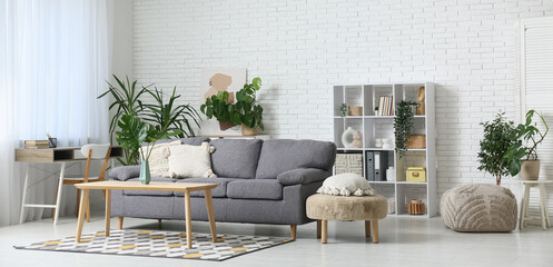 Modern interior of living room with tropical monstera leaves in vase on table and stylish sofa