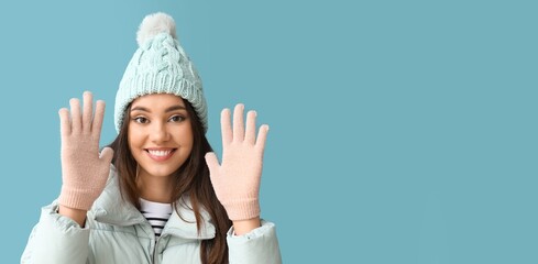 Young woman in warm gloves and hat on blue background with space for text