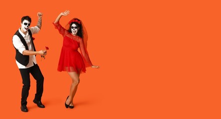 Dancing young couple with painted skulls on faces for Mexico's Day of the Dead (El Dia de Muertos) against orange background with space for text